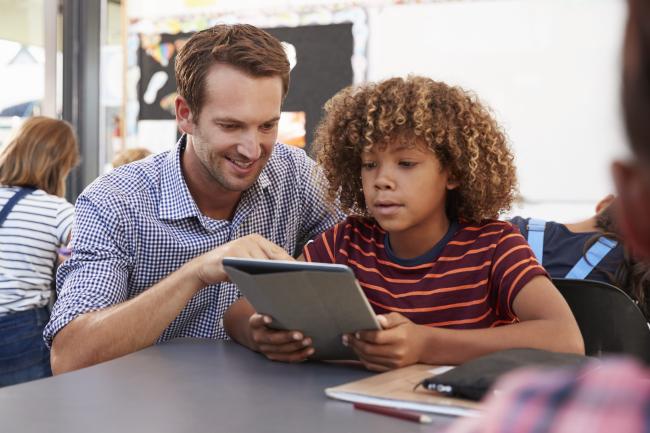 A male teacher helping an elementary school student complete an engaging assignment on a tablet